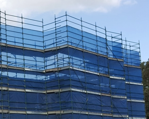 Scaffolding structure covered with blue safety mesh on a multi-level building site.